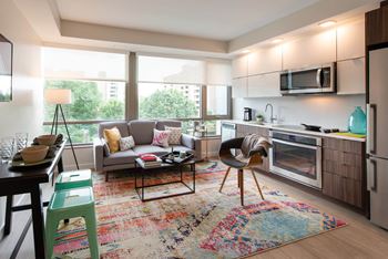 A modern kitchen and living room with a large window and a colorful rug.